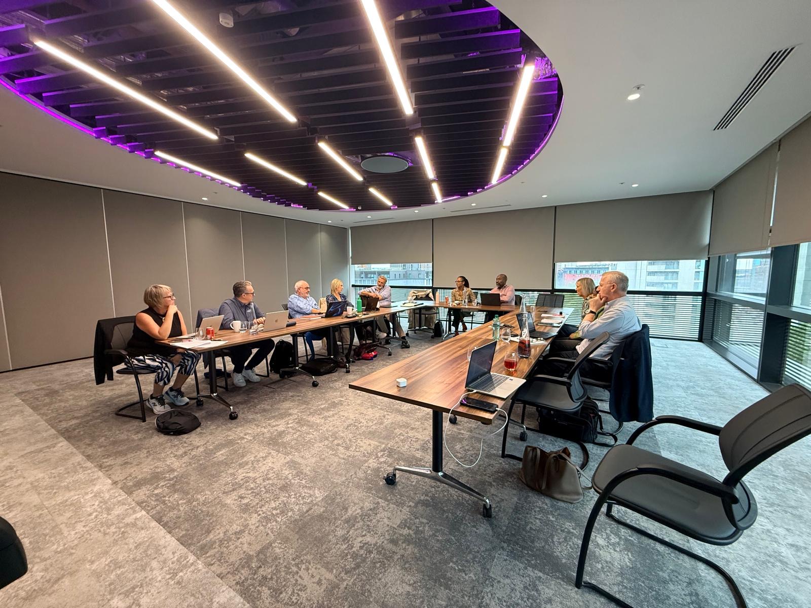 HPMA trustees seated around U-shaped tables in a bright meeting room, with laptops and notebooks open during an in-person strategy discussion.