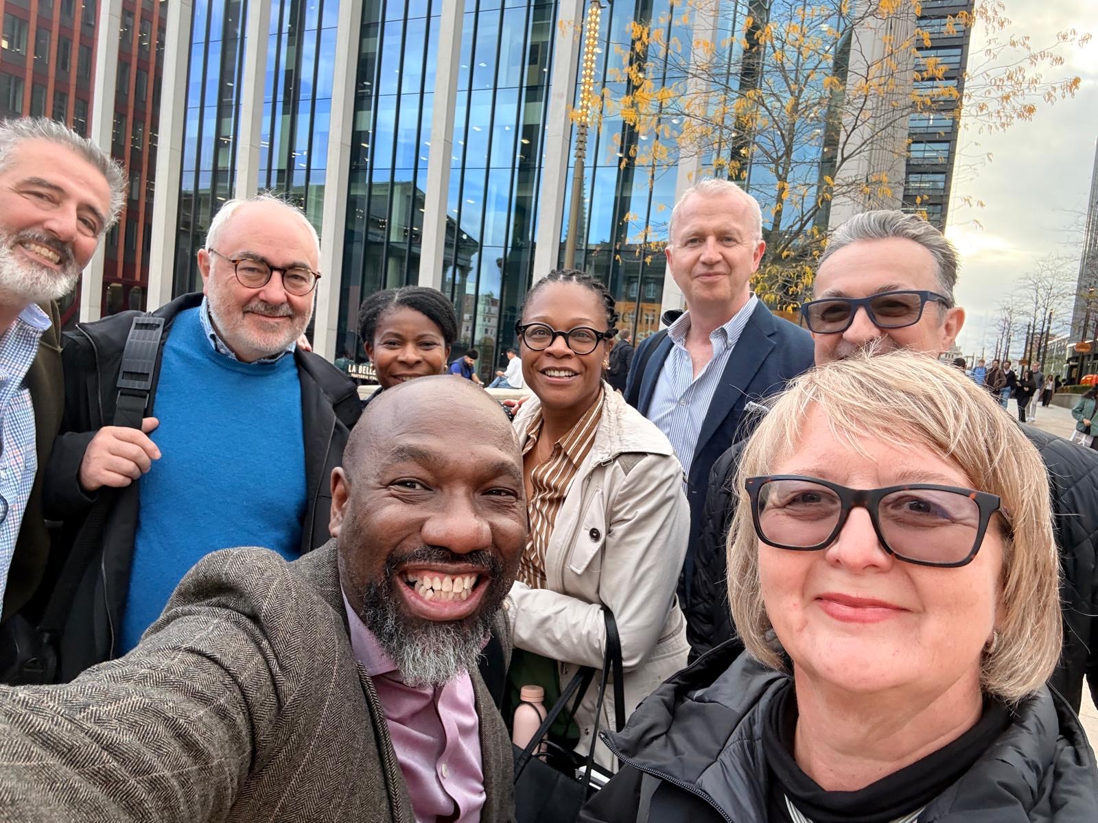 Janine La Rosa and colleagues smiling for a group selfie outside a modern glass-fronted building, with an autumn tree behind them.